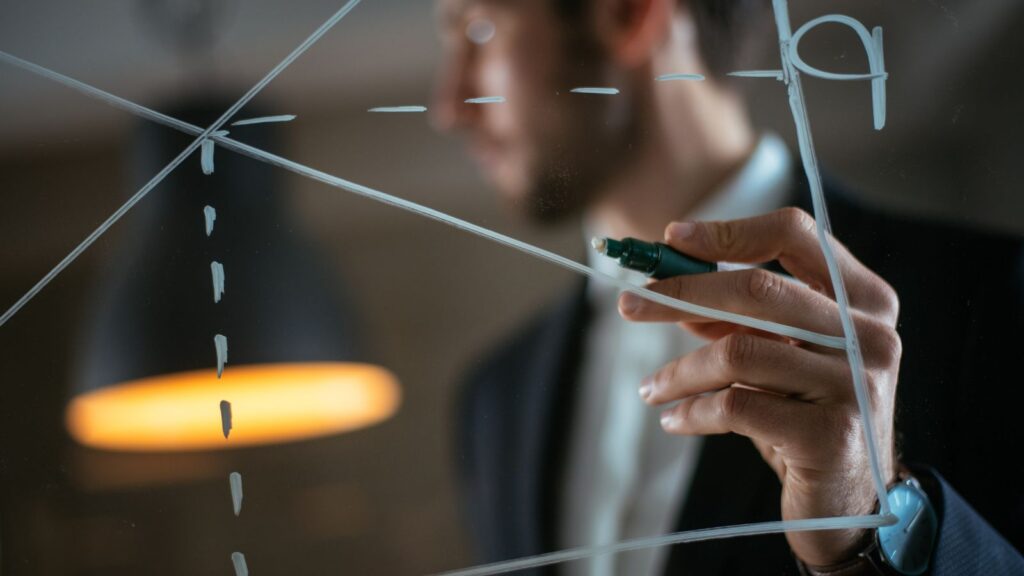 Man drawing supply-demand chart on glass wall