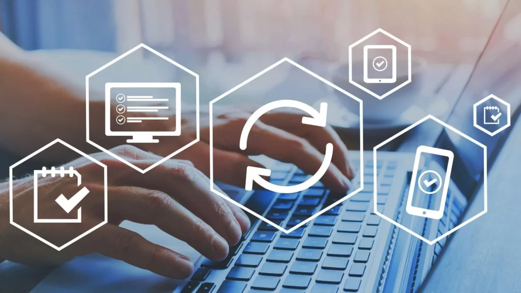 Hands typing on a laptop with overlay icons representing synchronization, checklists, and devices, symbolizing Microsoft Dynamics 365 BC updates and continuous system improvement.