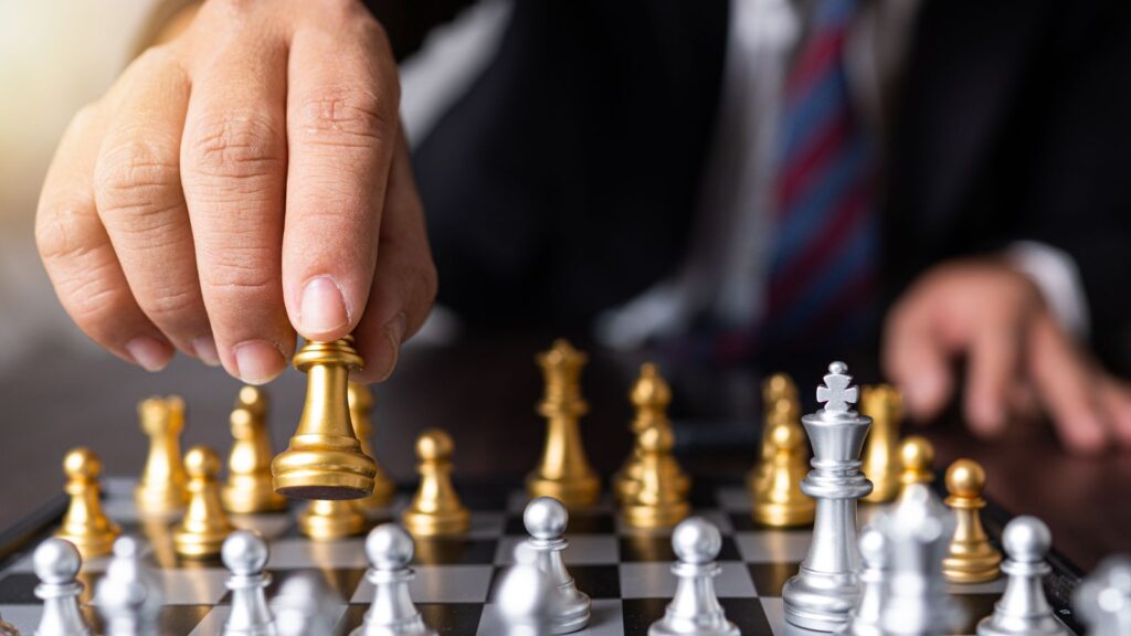 Close-up of a person in business attire moving a golden chess piece on a chessboard, symbolizing planning, strategy, and decision-making in business.