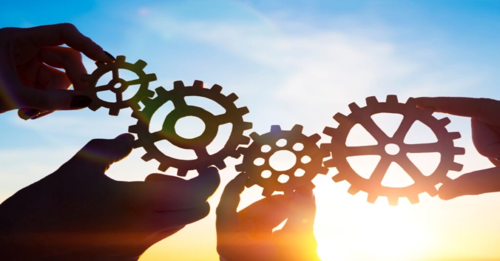 Four hands of businesspeople holding gears against the background of sunlight. The power pair