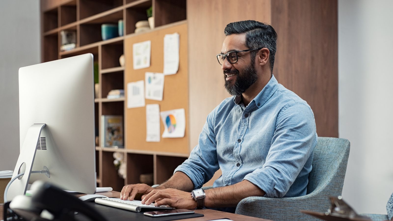 A professional man smiling while working at a desktop computer, symbolizing confidence and efficiency in mastering Microsoft Dynamics 365 Business Central basics for business operations.
